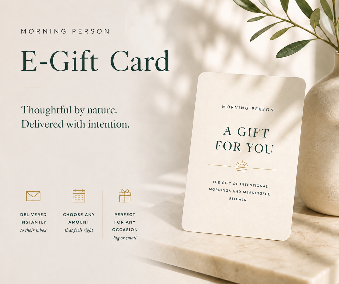 A Morning Person E-Gift Card displayed on a neutral beige surface next to a ceramic vase with green leaves. The card is cream-colored with dark green text reading &